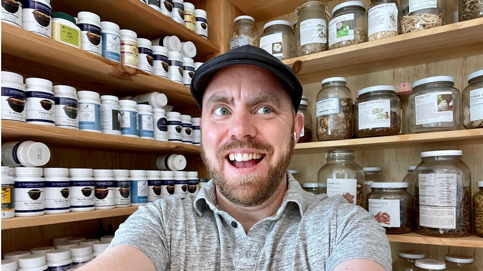 Eric Grey poses in front of shelf of Chinese herbs