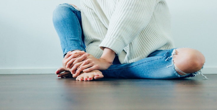 Woman sitting on floor and holding foot with hands