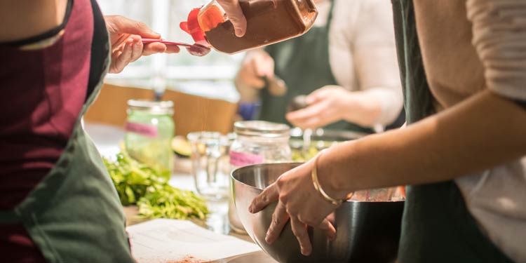 Hands pouring a spice and another person holding a bowl in a cooking class environment