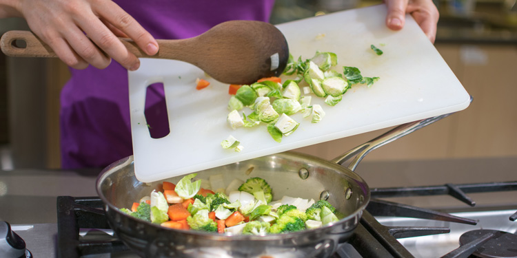 cook tossing brussels sprouts and carrots into a pan
