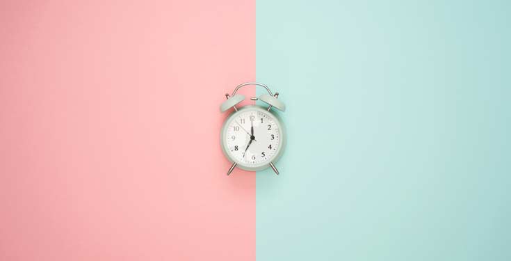 Old school alarm clock in the middle of a pale pink and sky blue background