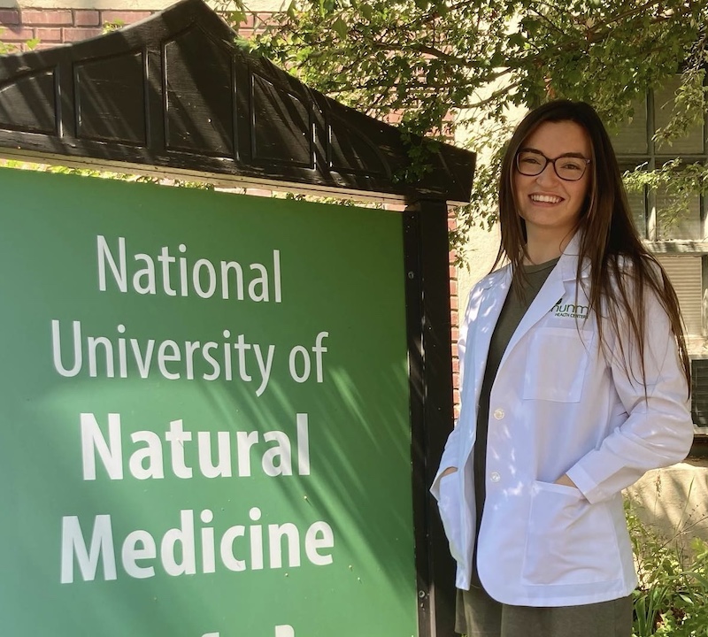 An NUNM student poses next to an NUNM sign during their White Coat Ceremony