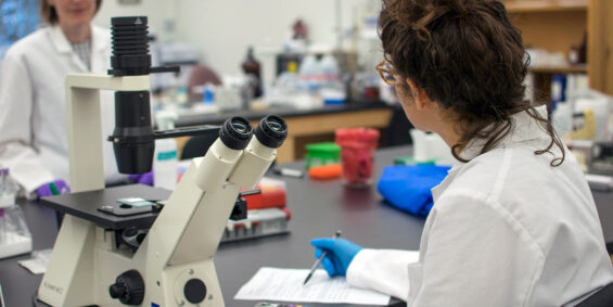 Woman in white coat working at a microscope in a lab