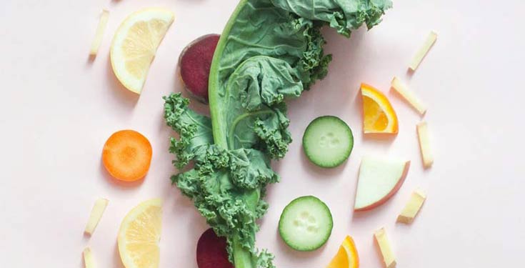 slices of lemon, beets, carrots, cucumbers around a kale leaf