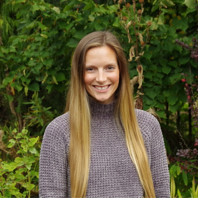 taylor boham smiling for a photo swearing a purple sweater with plants in the background