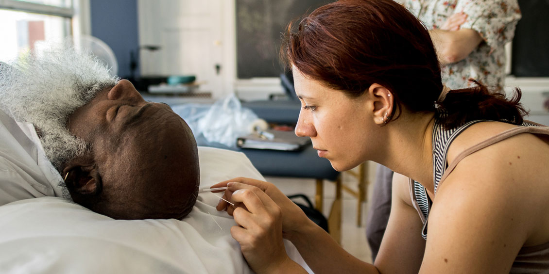 Woman, on right, putting acupuncture needle into man's head